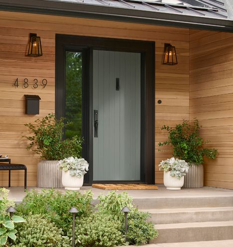 two planters with flowers are on the steps to a front door that is made of wood