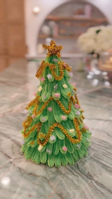 a small green christmas tree sitting on top of a marble counter next to a vase filled with flowers