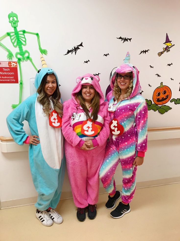 three women in costumes standing next to each other with halloween decorations on the wall behind them