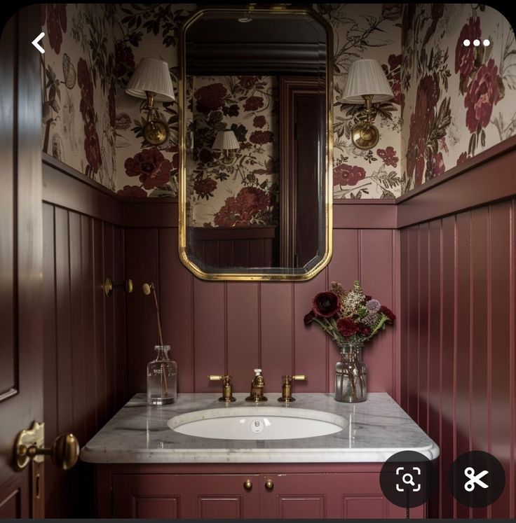 a bathroom with red walls and floral wallpaper, gold fixtures and marble countertop