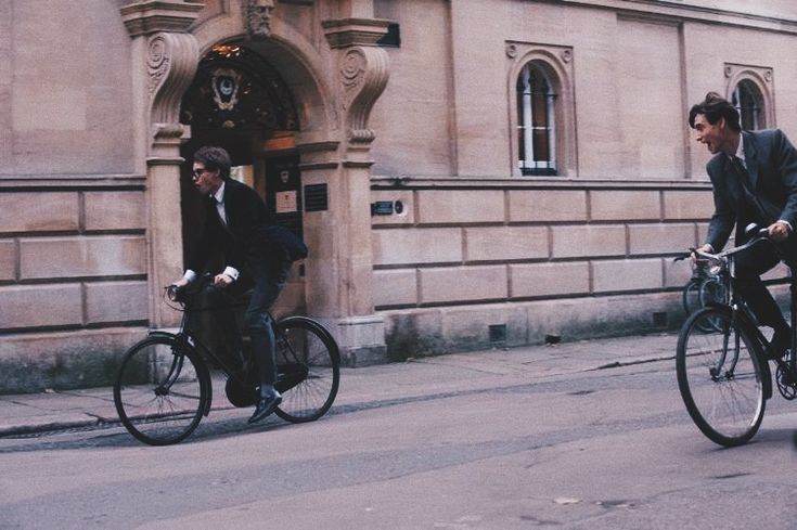 two men riding bikes in front of a building