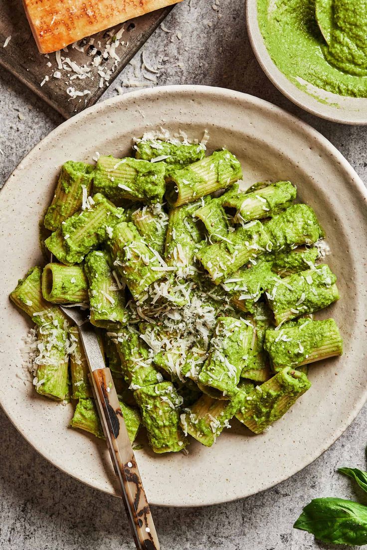 a white plate topped with green food next to two bowls filled with pesto sauce