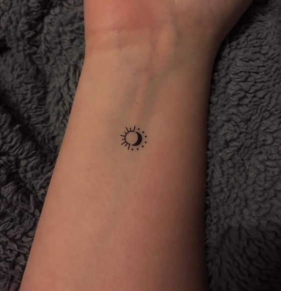 a woman's wrist with a small sun and moon tattoo on the left arm