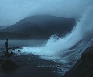 a man standing on top of a beach next to the ocean under a cloudy sky