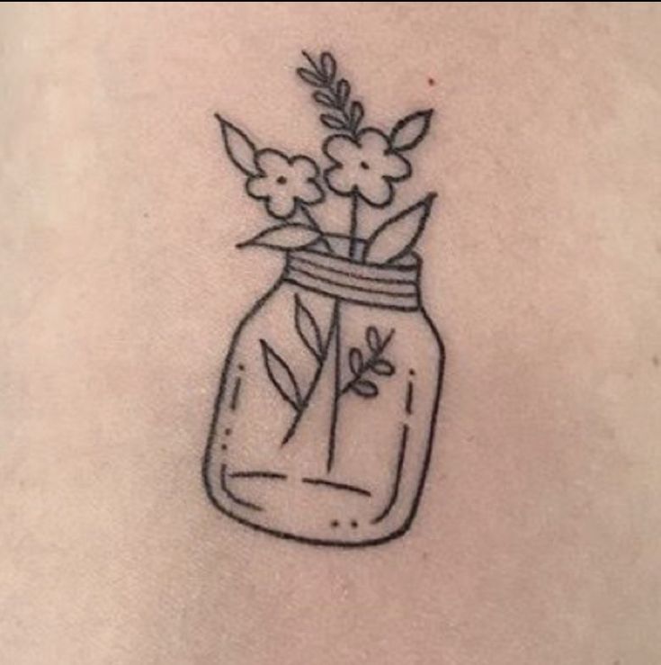 a small jar with flowers in it on the back of a woman's shoulder