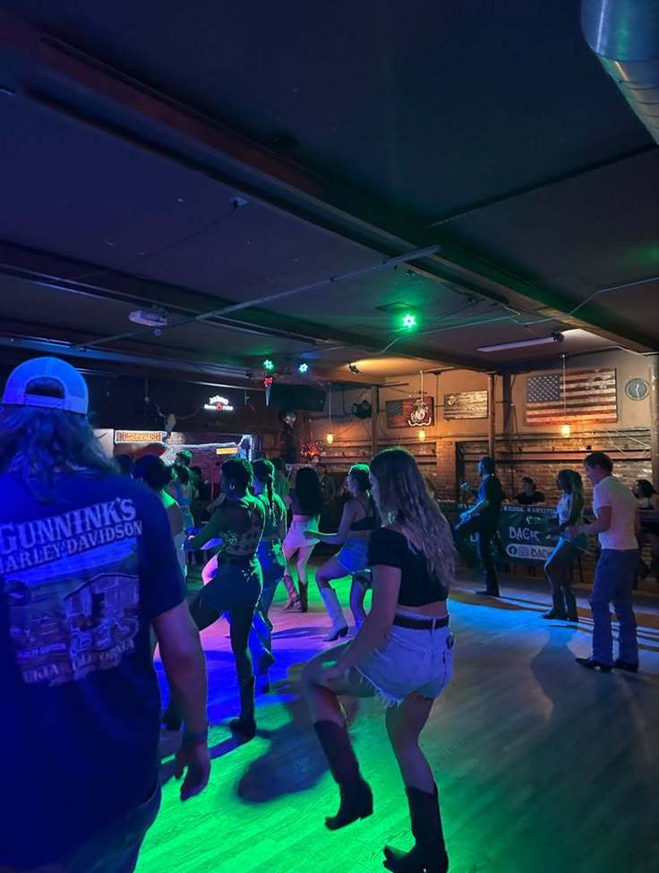 a group of people standing around in a room with neon lights on the dance floor