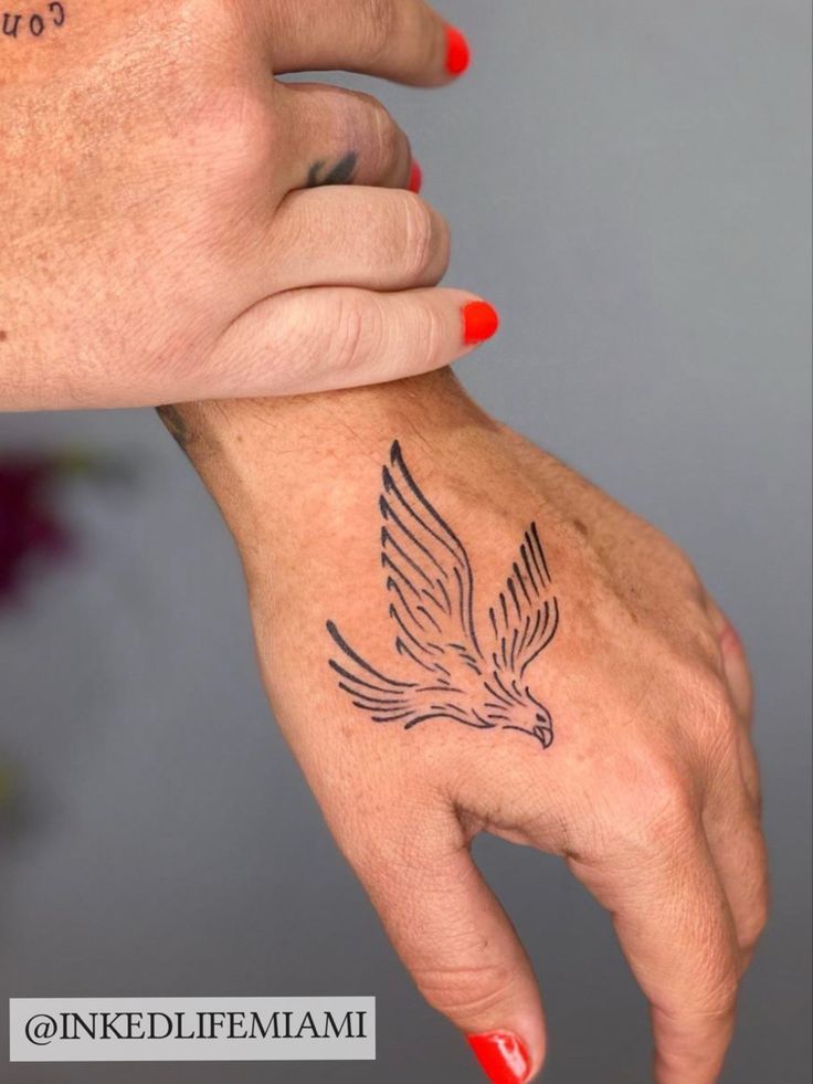 two hands are holding each other with tattoos on their wrists and fingers, one has a bird tattoo on it's left hand