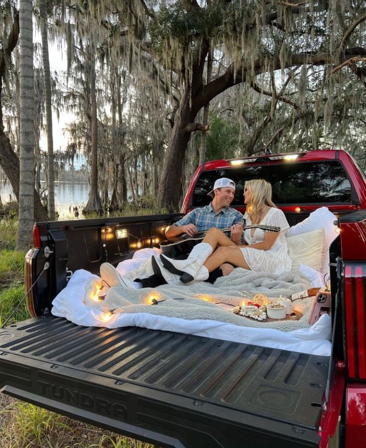 a man and woman sitting in the back of a truck with lights on it's bed