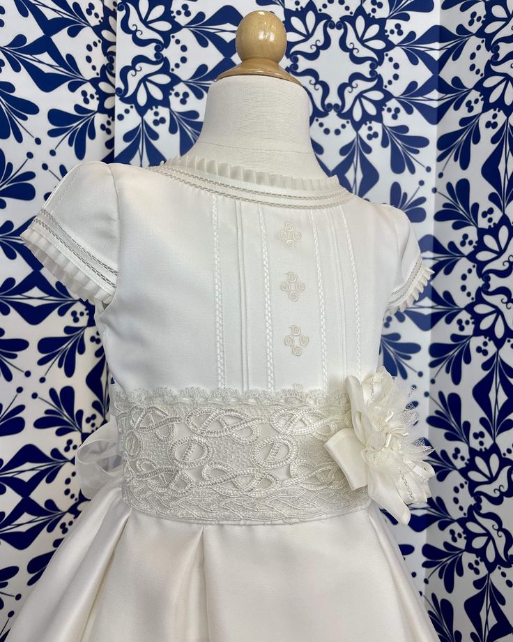 A traditional off-white dress with pleats and little roses embroidered on the front of the body, the sash has gorgeous lace on the sash. The skirt has beautiful details throughout. The flower is an applique, which can be removed at any time. It has covered buttons on the back for closure and a bow. Made in Spain Dry Clean 100% silk Final sale, no exchanges nor returns are available First Communion Dress, Dress With Pleats, First Communion Dresses, Off White Dresses, Dresses For Girls, Communion Dresses, Dresses 2024, First Communion, Dress First