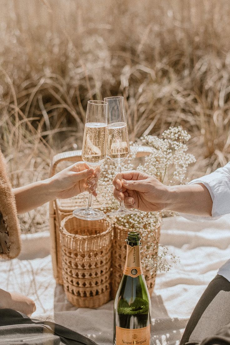 two people toasting with wine glasses on a picnic table in front of some flowers