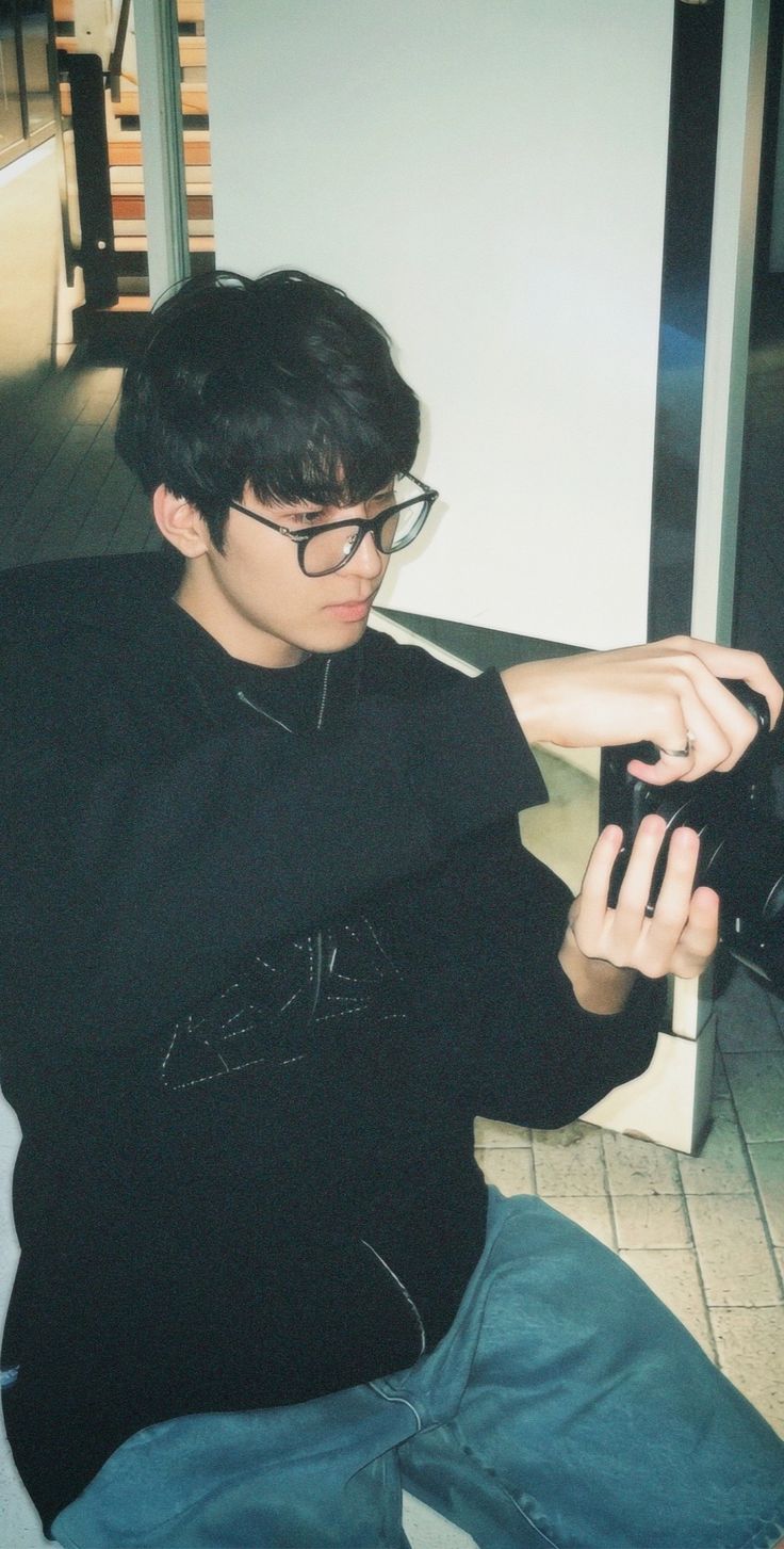 a young man sitting on the floor holding a camera in his hand and looking at it