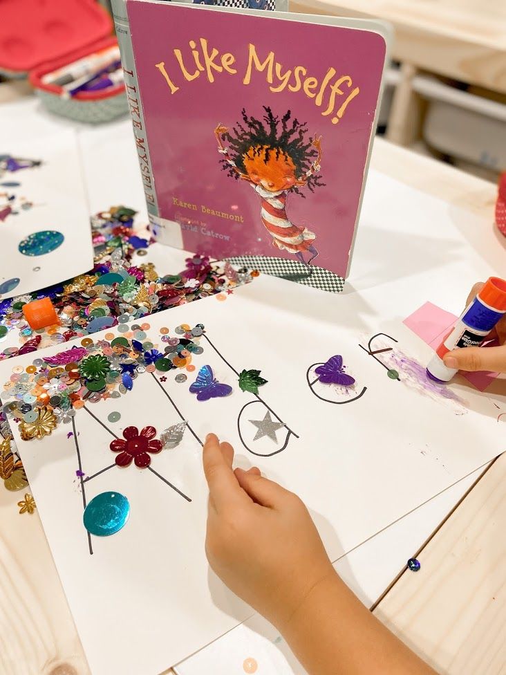 a child's hand is on the table with some crafting materials and a book