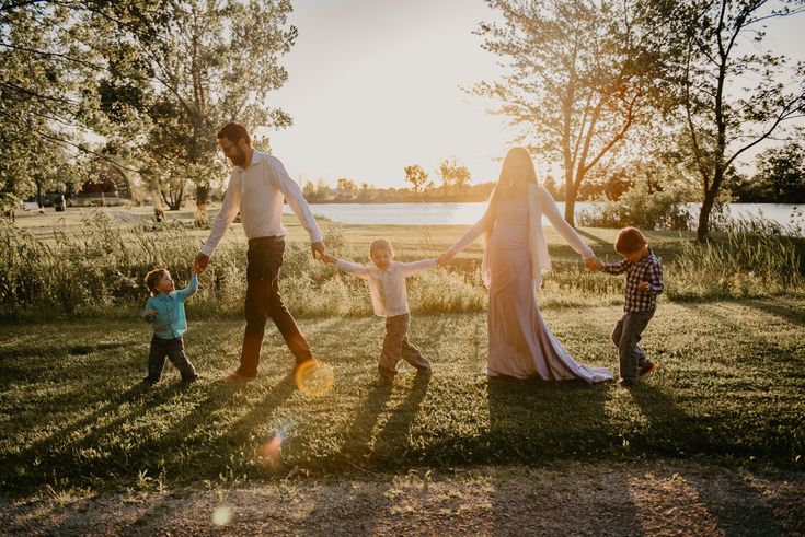 a family holding hands and walking in the grass with their two children, one is wearing a long white dress