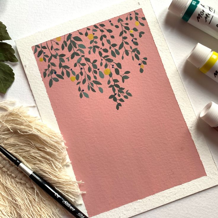 some paint and markers are laying on top of a piece of pink paper with leaves