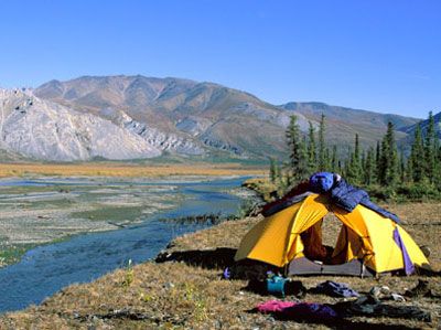 a yellow and blue tent sitting on top of a grass covered field next to a river