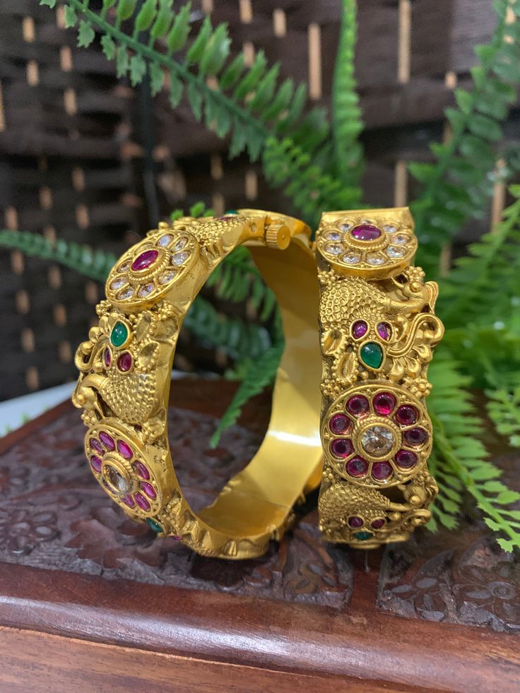 Temple bangle in matte gold and ruby stone. Detailing has the Rajasthani similarity. About an inch wide. Disclaimer: Price listed is for a single Kada. If you want to get them in a pair please select quantity 2. Gold Bracelet With Peacock Design As Gift, Gold Bracelets With Peacock Design As Gift, Festive Gold Bangle With Stone Setting, Festive Gold Bangle With Peacock Design, Festive Gold Bracelets With Stone Setting, Festive Gold Bracelets With Peacock Design, Traditional Gold Bangle With Ruby, Gold Bracelet With Stone Setting For Festive Occasion, Traditional Gold Ruby Bangle