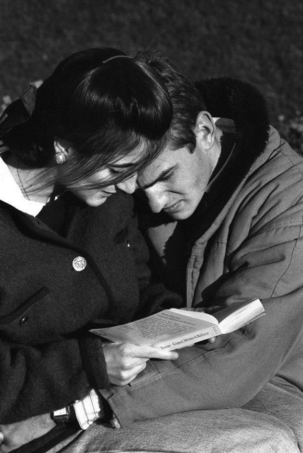 a man and woman sitting next to each other on the ground looking at a book