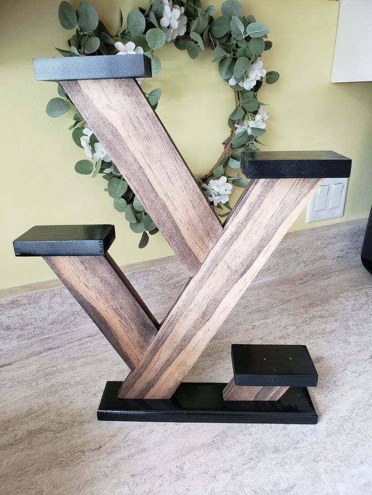 a wooden letter shaped sculpture sitting on top of a floor next to a vase filled with flowers