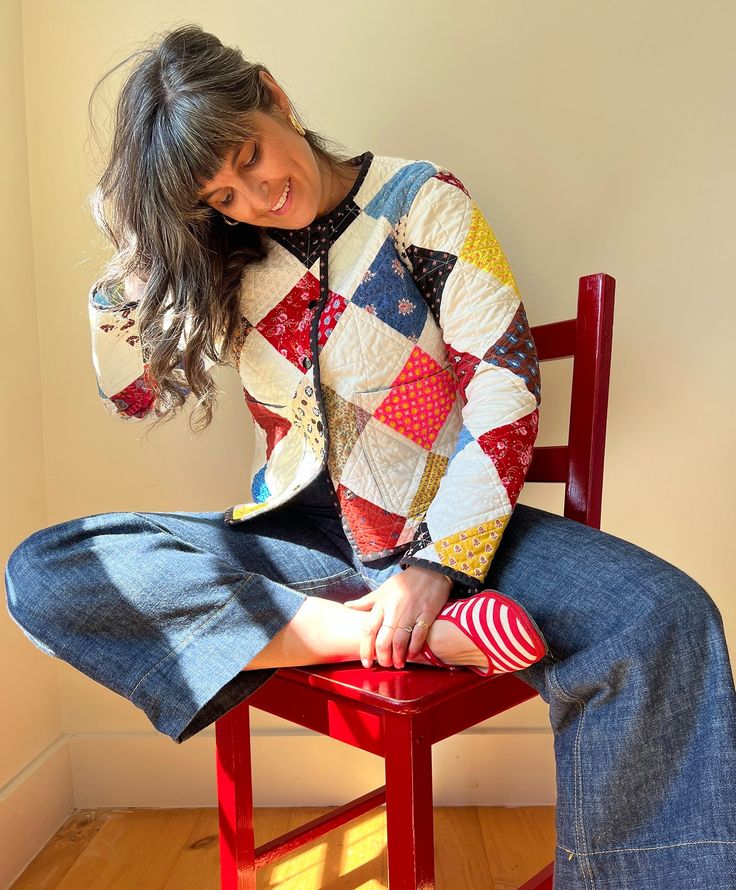 a woman sitting on top of a red chair wearing a quilted jacket and striped socks