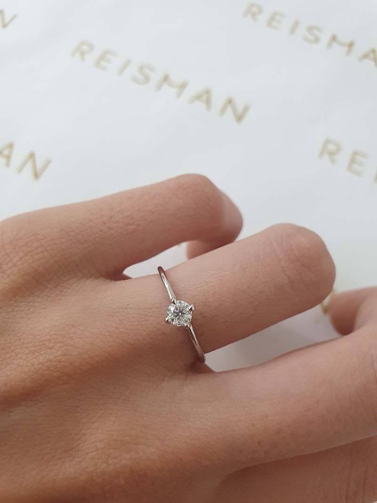 a woman's hand with a diamond ring on top of her finger, next to a book