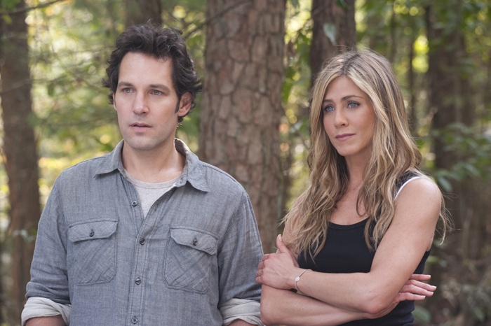 a man and woman standing in front of trees with their arms around each other, looking at the camera