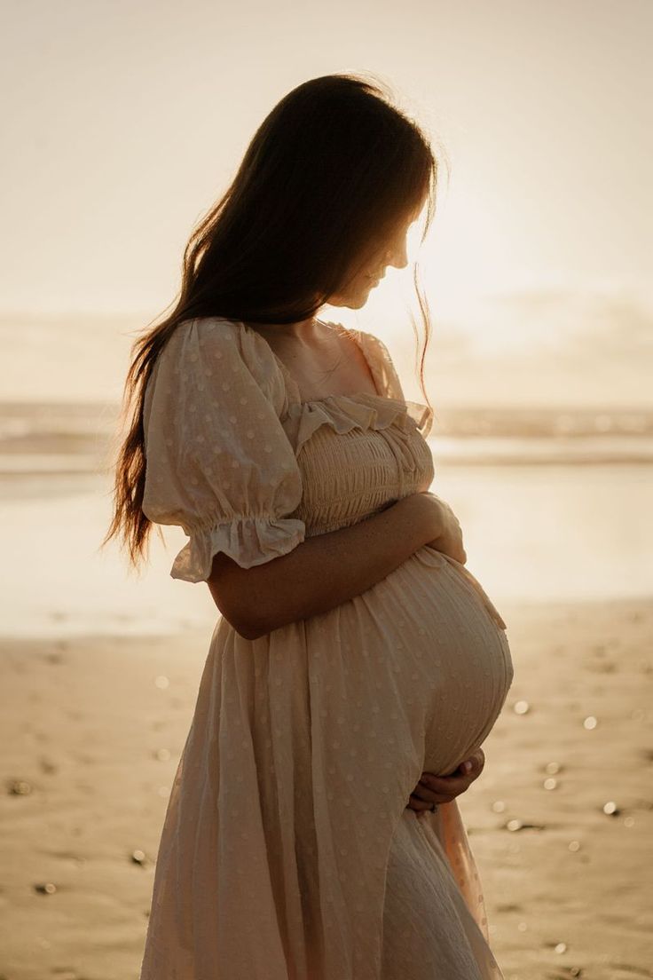 a pregnant woman standing on the beach at sunset