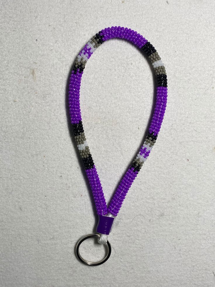 a purple and black lanyard with a metal hook on the end that is attached to a white wall