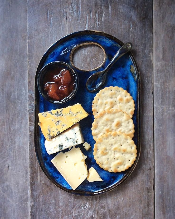 a blue plate topped with crackers, cheese and jam on top of a wooden table