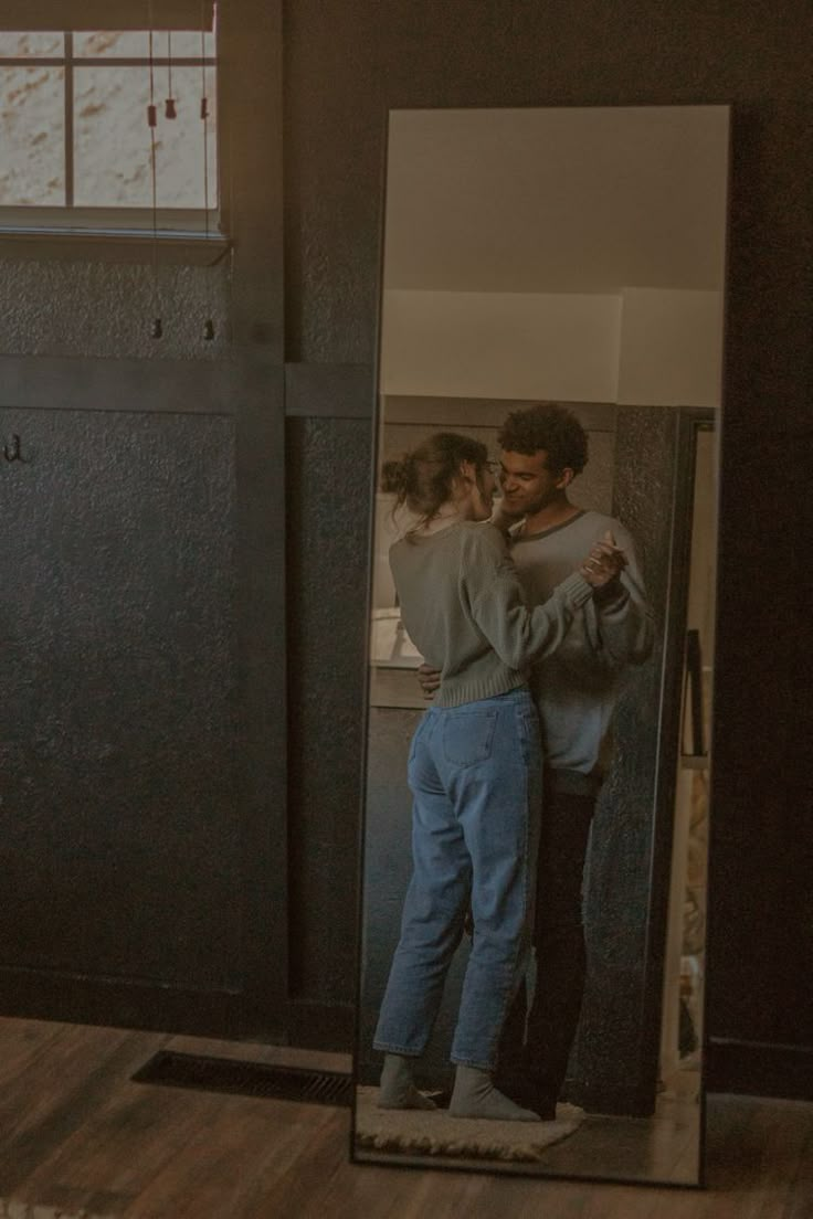 a man and woman standing in front of a mirror with their arms around each other