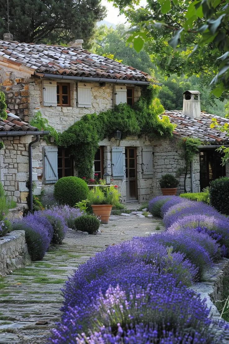 an old stone house with lots of lavender in the foreground and trees around it