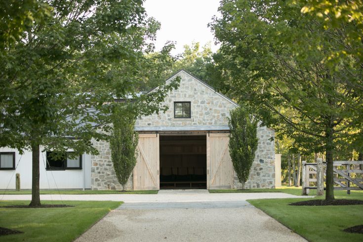 a stone barn with trees surrounding it and a walkway leading up to the front door