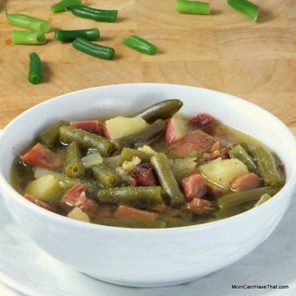 a white bowl filled with soup on top of a wooden table next to green beans