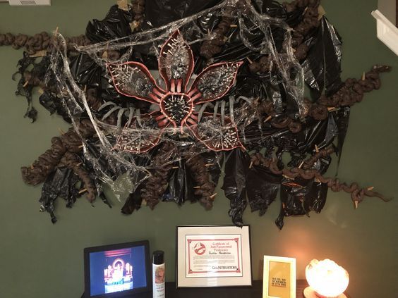 a computer desk topped with a laptop computer next to a spider web covered wall hanging