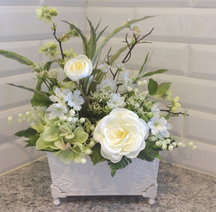 a white vase filled with flowers on top of a marble counter next to a wall