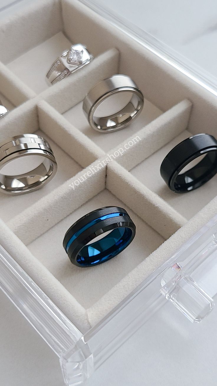 six different rings in a clear box on top of a white table with other items