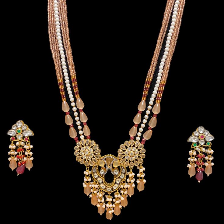 Our Peach Samaa Kundan Long Necklace Set is a modern take on the classic. Its meticulously handcrafted design showcases an intricate pendant with a Tyaani Kundan with black and gold finish. All Tyaani Kundans have gold foiling. The pendant also features AAA Quality American Diamonds with dropping of peach beads. The necklace is made of a string of pearls surrounded on both sides by peach onyx and maroon beads. Specifications Materilas Used: Tyaani Kundan with gold foiling, AAA Quality American D Kundan Long Necklace, Long Necklace Set, String Of Pearls, Onyx Bead, Temple Jewellery, American Diamond, Showcase Design, Black And Gold, Long Necklace