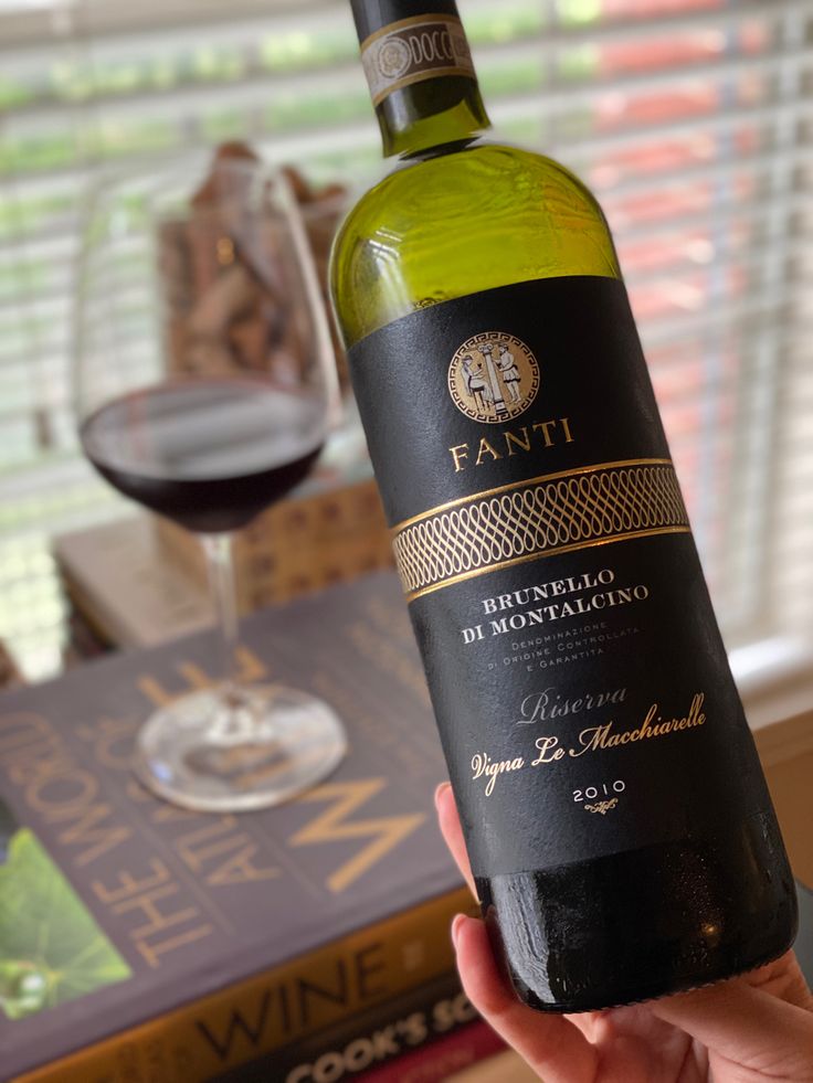 a person holding up a bottle of wine in front of a table with books and a glass of wine