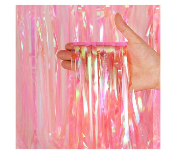 a hand holding a pink comb in front of a wall covered with plastic streamers