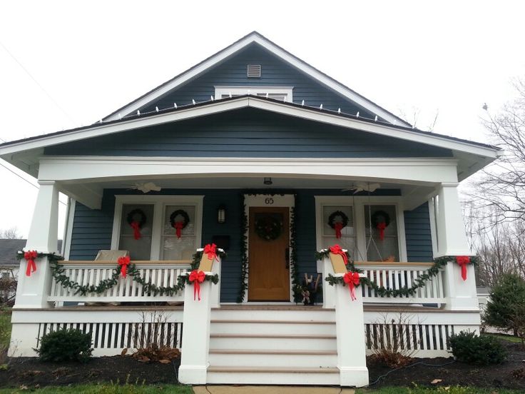 a blue house decorated for christmas with wreaths on the front porch and red bows