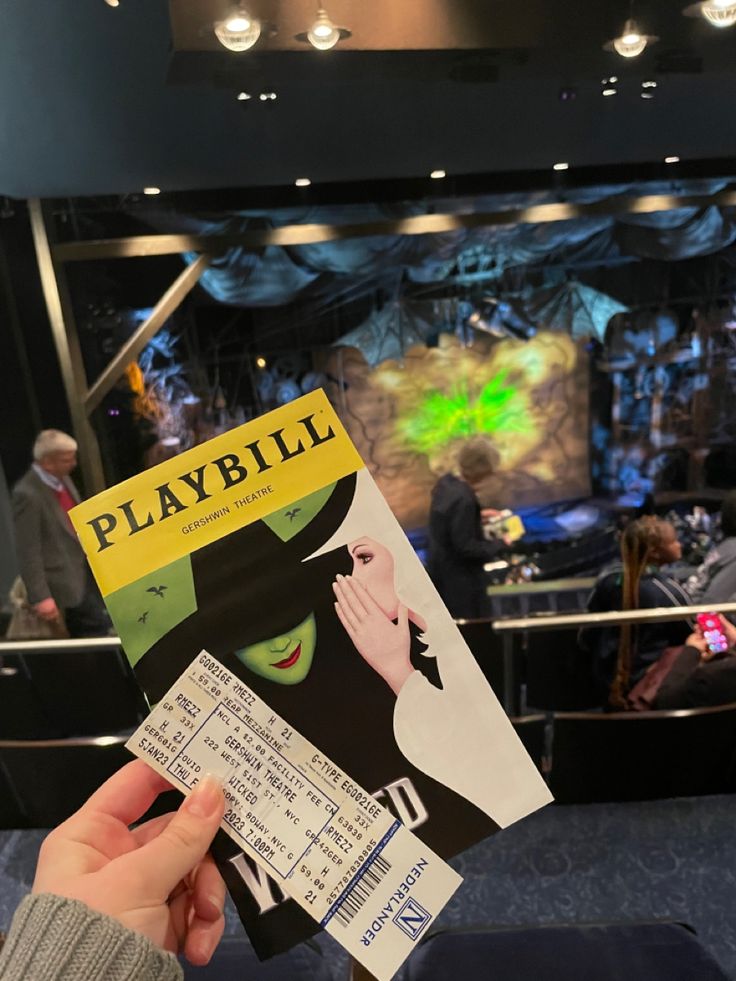 a person holding up a playbill ticket in front of a stage