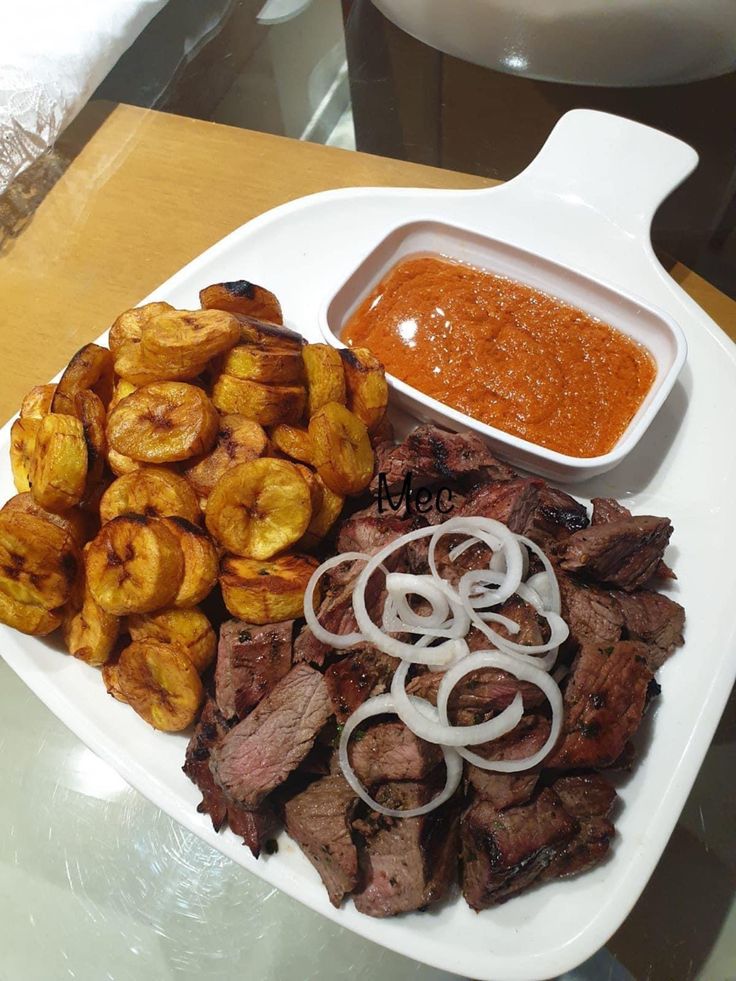 a white plate topped with meat and veggies next to a bowl of sauce