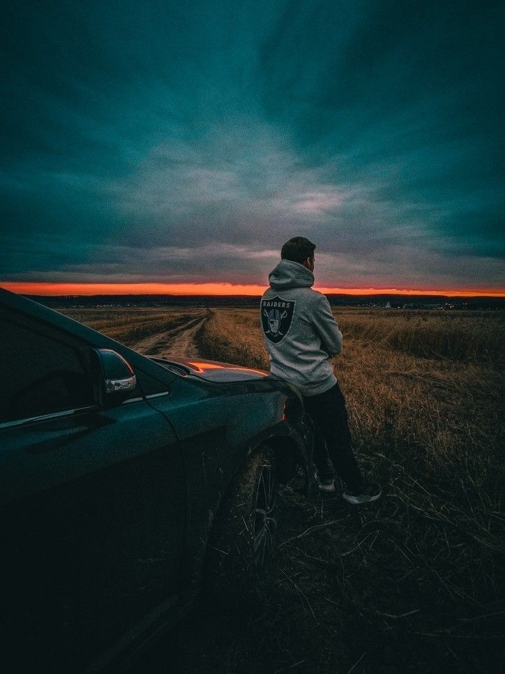 a person standing next to a car on the side of a road at night time