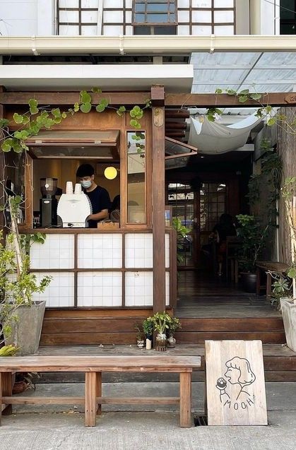 a man sitting at a table in front of a building with potted plants on it