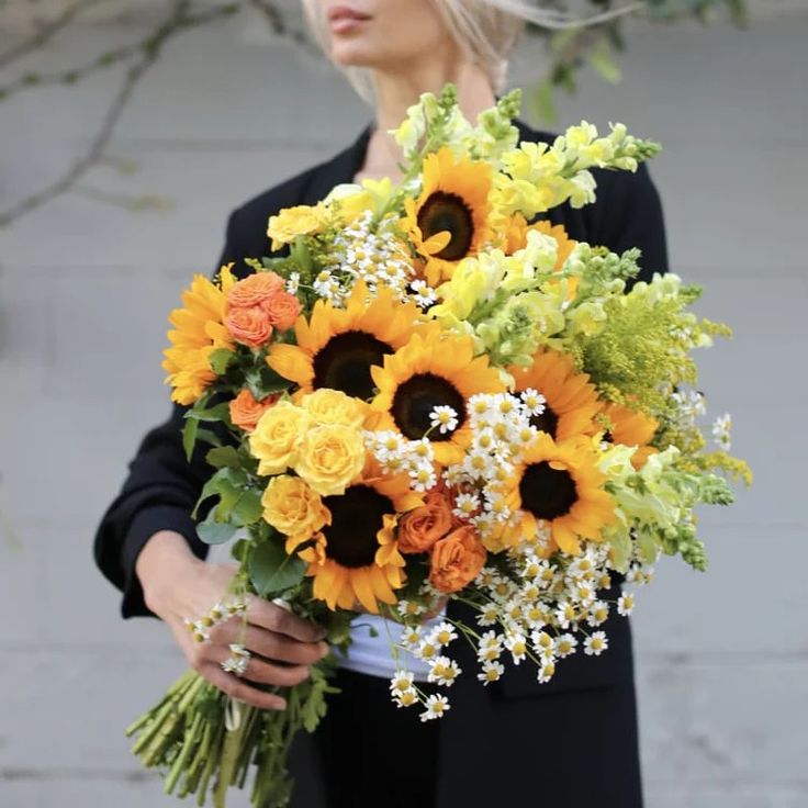 a woman holding a bouquet of sunflowers and other flowers