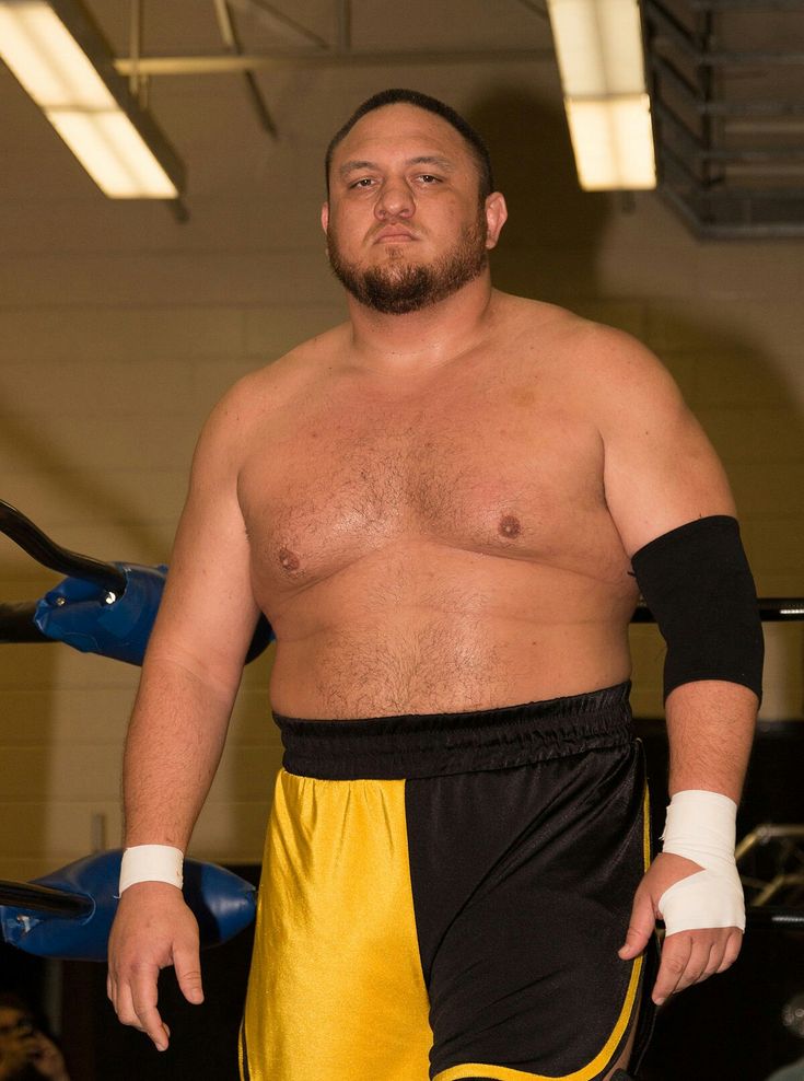 a man with no shirt on standing next to a blue and yellow object in a gym