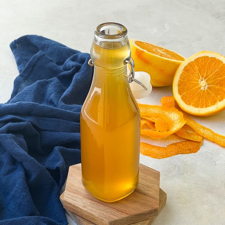 a bottle of orange juice sitting on top of a cutting board next to sliced oranges