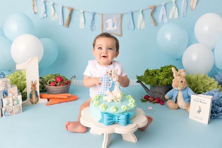 a baby is sitting in front of a cake with an animal on it, surrounded by balloons and decorations