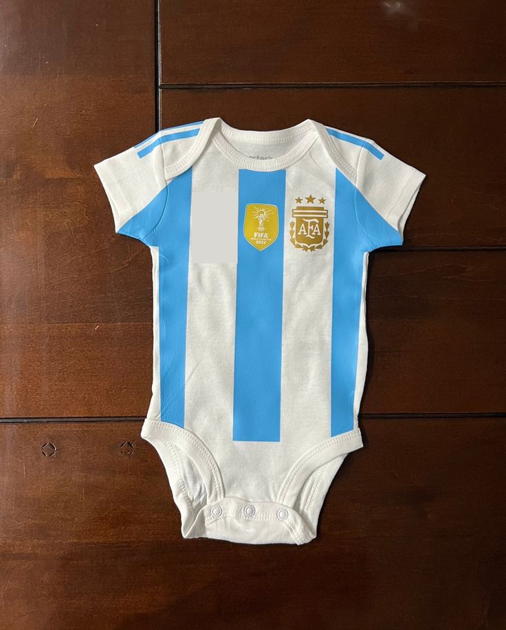 a blue and white striped baby bodysuit sitting on top of a wooden floor next to a wall