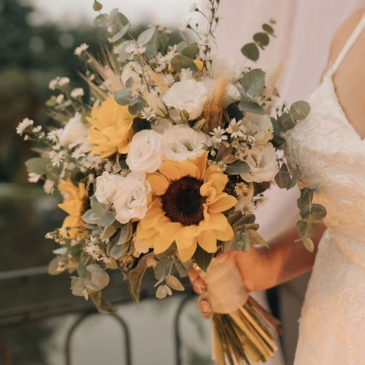 a bride holding a bridal bouquet with sunflowers and greenery in her hand