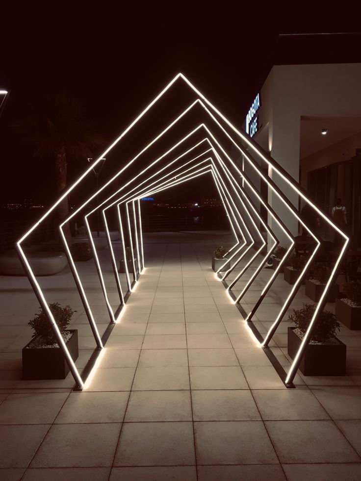 an illuminated walkway in the middle of a building with potted plants on either side